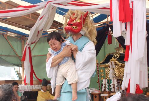 鬼の面を被った人に抱えられた子どもが泣いています